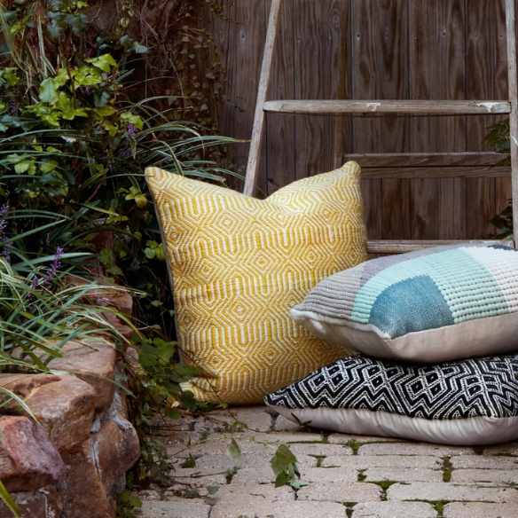 Yellow and cream geometric throw pillow on a bright outdoor chair with summer decor