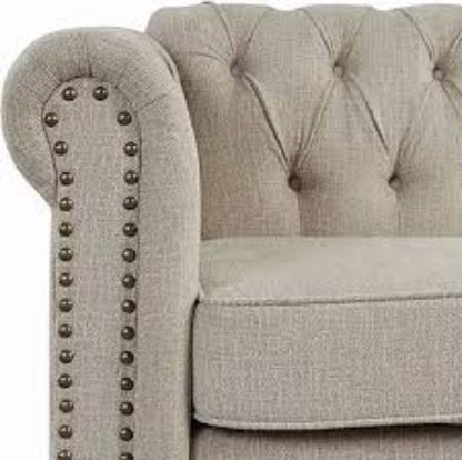 A warm beige mid-century modern accent chair with hand-pulled tufted buttons, silver-toned nailhead accents, and turned wooden legs. The chair features a plush, ergonomic design with foam cushioning and a tufted back for added texture and sophistication. The solid rubberwood frame and durable upholstery ensure long-lasting comfort and support, making it perfect for various rooms including the living room, office, or bedroom.