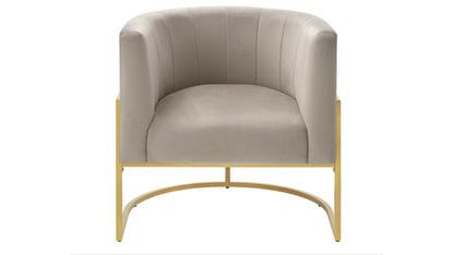 Taupe velvet barrel accent chair with gold accents and a hidden, storable ottoman. Features flared arms, foam-filled seat and back for comfort, a solid wood frame with a sled base for stability, and includes toss pillows for added comfort. The ottoman conveniently tucks under the chair to save space, creating a stylish, space-saving solution for any room.