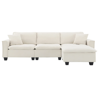 Beige suede L-shaped sectional sofa with removable ottoman, tufted seat cushions, and two matching accent pillows