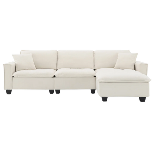 Beige suede L-shaped sectional sofa with removable ottoman, tufted seat cushions, and two matching accent pillows