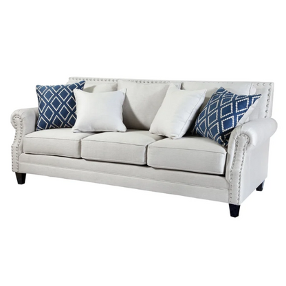 Beige tufted linen sofa with rolled arms, nailhead trim, tapered wooden legs, and accent pillows in transitional style.

