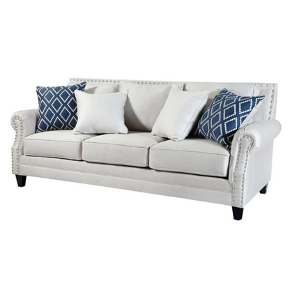 Beige tufted linen sofa with rolled arms, nailhead trim, tapered wooden legs, and accent pillows in transitional style.

