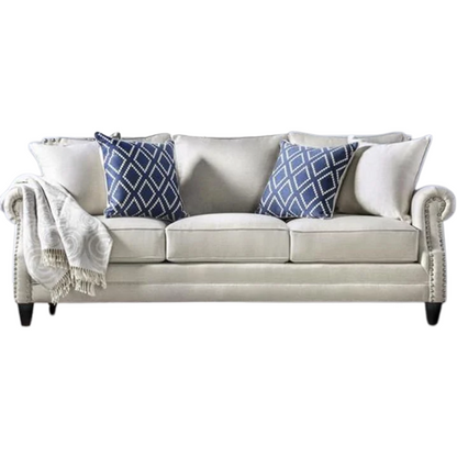 Beige tufted linen sofa with rolled arms, nailhead trim, tapered wooden legs, and accent pillows in transitional style.

