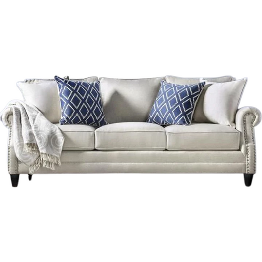 Beige tufted linen sofa with rolled arms, nailhead trim, tapered wooden legs, and accent pillows in transitional style.

