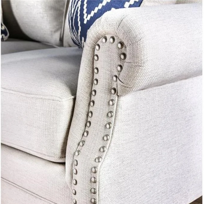Beige tufted linen sofa with rolled arms, nailhead trim, tapered wooden legs, and accent pillows in transitional style.

