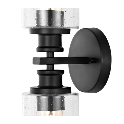 Art Deco-style black wall sconce with dual clear seeded glass cylinder shades and Edison-style LED bulbs, suitable for bathroom or hallway lighting

