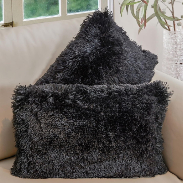 Set of two black faux fur throw pillows with white-tipped shaggy texture on a modern neutral-toned sofa


