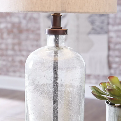 Bronze-tone seeded glass table lamp with beige fabric drum shade, featuring a metal base and compact design for modern farmhouse or industrial interiors

