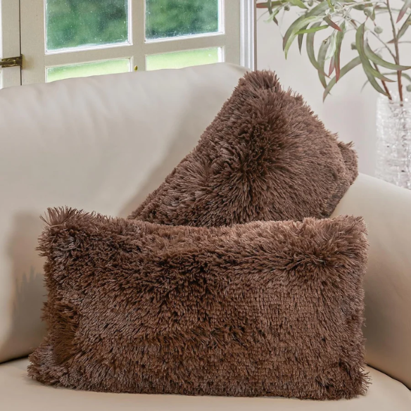 Set of two brown faux fur throw pillows with plush shaggy texture on a rustic wood-accented couch

