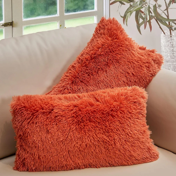 Set of two burnt orange faux fur throw pillows with shaggy texture on a modern sofa

