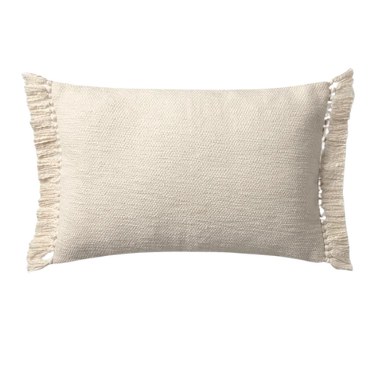 Cream lumbar throw pillow with soft fringe trim, rectangular 13x21 design, made from neutral cotton blend fabric, styled on a sofa for cozy, modern home decor.

