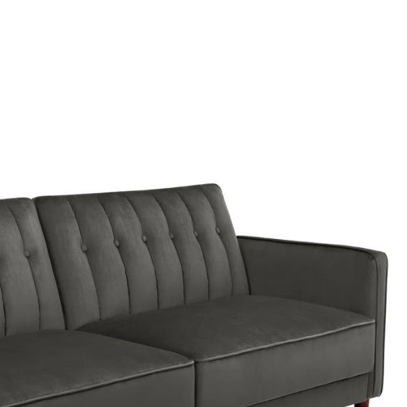 Dark grey velvet convertible sofa with vertical tufting, split-back design, square arms, and brown tapered legs, convertible into a twin-size sleeper.