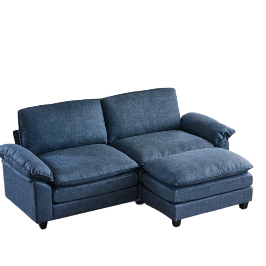 Denim blue modular cloud sofa with deep cushioned seating, curved pillow arms, and free-standing ottoman