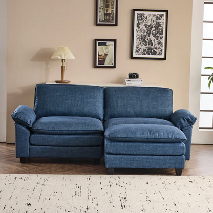Denim blue modular cloud sofa with deep cushioned seating, curved pillow arms, and free-standing ottoman