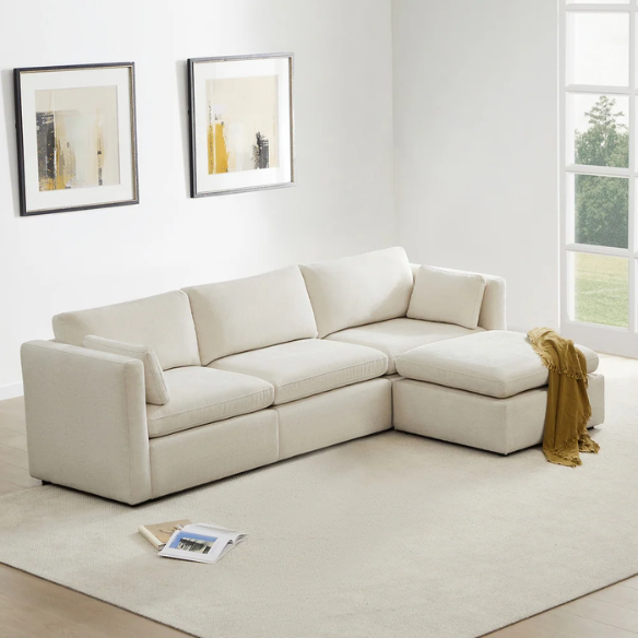 Beige modular four-piece sectional sofa with wide seats, soft chenille fabric, removable cushions, and built-in storage ottoman — ideal for modern and adaptable living room layouts.

