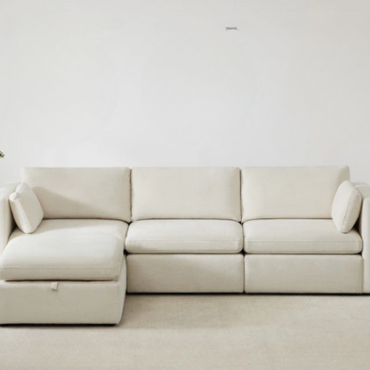 Beige modular four-piece sectional sofa with wide seats, soft chenille fabric, removable cushions, and built-in storage ottoman — ideal for modern and adaptable living room layouts.

