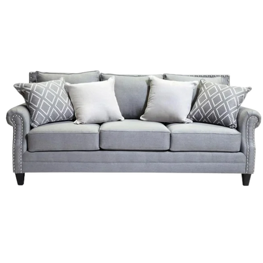 Grey tufted linen sofa with rolled arms, nailhead trim, tapered wooden legs, and accent pillows in a transitional design.

