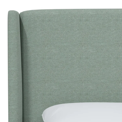 Light green linen upholstered king size bed with foam-padded wingback headboard, black low-profile metal legs, and sturdy wood frame.

