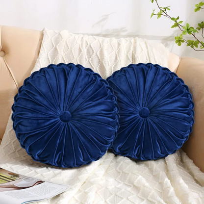 Navy blue velvet round throw pillows with hand-sewn pleats and button center, 14.5-inch set of two styled on a neutral-toned sofa.

