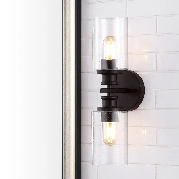 Oil-rubbed bronze wall sconce with dual clear seeded glass cylinder shades and Edison-style LED bulbs, perfect for rustic, farmhouse, or traditional interiors

