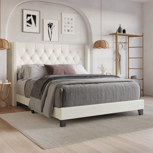 Beige queen-size bed with faux leather upholstery, wingback tufted headboard, nailhead trim, and low-profile wooden frame.

