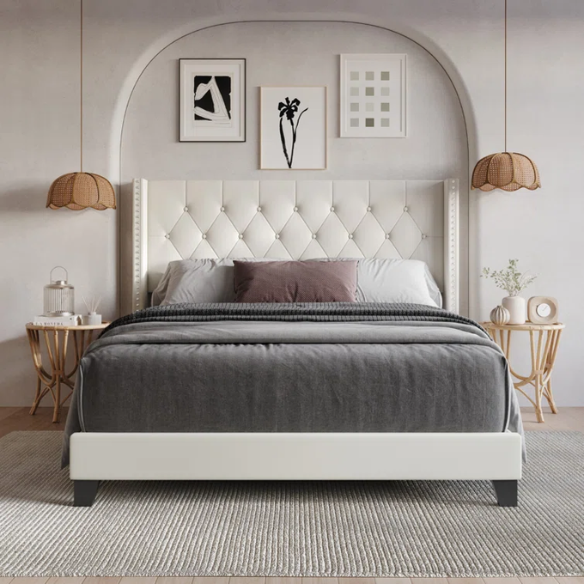 Beige queen-size bed with faux leather upholstery, wingback tufted headboard, nailhead trim, and low-profile wooden frame.


