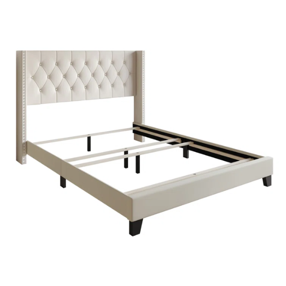Beige queen-size bed with faux leather upholstery, wingback tufted headboard, nailhead trim, and low-profile wooden frame.

