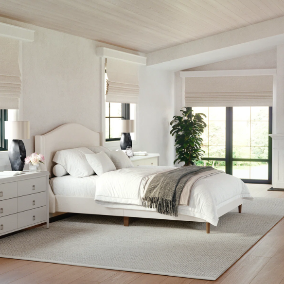 Full-size beige upholstered platform bed with curved wingback headboard, cushioned side rails, and tapered wooden legs, shown in a modern bedroom setting.


