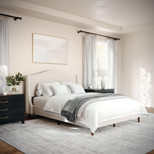 Full-size beige upholstered platform bed with curved wingback headboard, cushioned side rails, and tapered wooden legs, shown in a modern bedroom setting.

