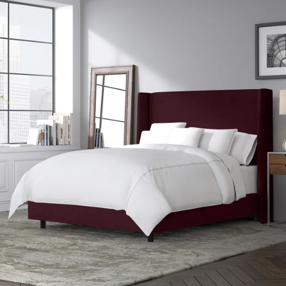 Burgundy king-size upholstered bed in velvet fabric with wingback headboard and low-profile black metal legs.


