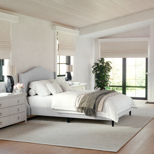 Full-size grey upholstered platform bed with curved wingback headboard, cushioned side rails, and tapered wooden legs in a stylish modern bedroom.

