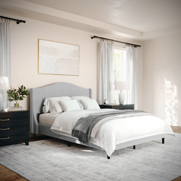 Full-size grey upholstered platform bed with curved wingback headboard, cushioned side rails, and tapered wooden legs in a stylish modern bedroom.

