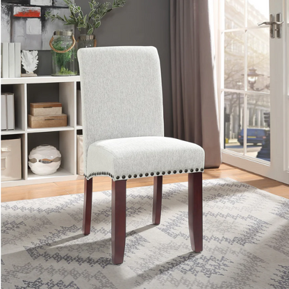 Light grey upholstered Parsons chair with scrolled high back, antique bronze nailhead trim, and solid wood legs