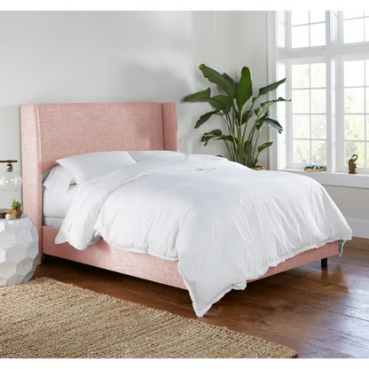 Rosy pink king-size upholstered bed in linen with wingback headboard and black metal legs.

