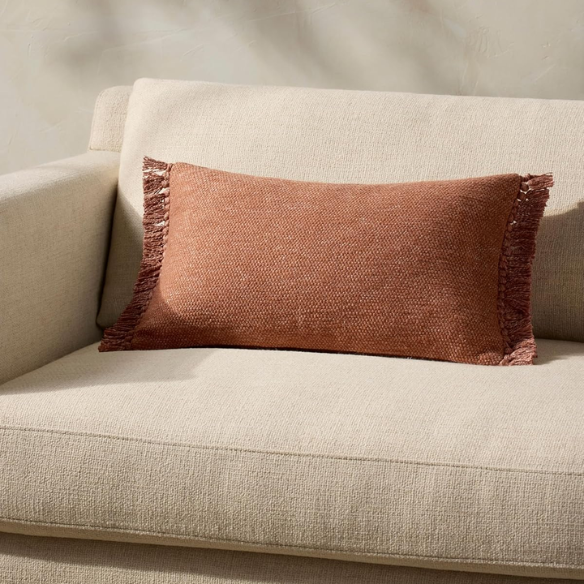 Rust-colored rectangular lumbar throw pillow with fringe trim, 13x21 inches, featuring a cotton-polyester-rayon cover and plush polyester fill—ideal for modern or boho home décor.

