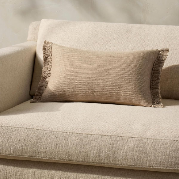 Tan rectangular lumbar throw pillow with fringe, 13x21 inches, made from a cotton-polyester-rayon blend and filled with plush polyester—perfect for neutral, modern, or boho interiors.

