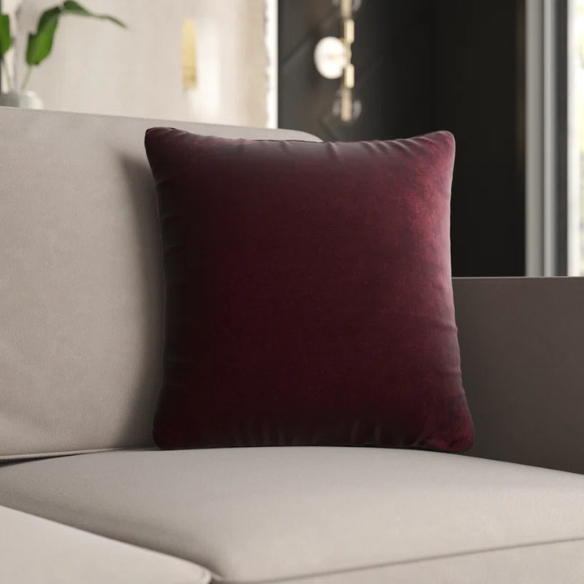 Red wine crushed velvet throw pillow, 16x16 square with soft, reversible fabric and hidden zipper, styled on a modern sofa for a sophisticated touch.

