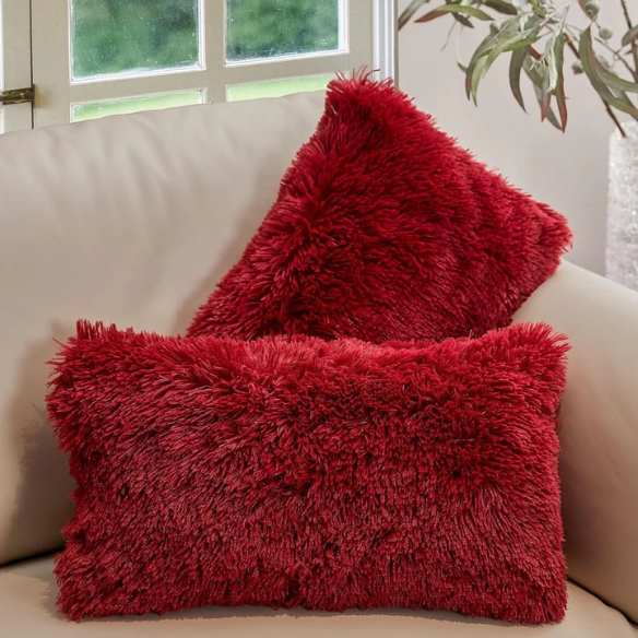 Set of two red wine faux fur throw pillows with plush shaggy texture on a modern velvet sofa

