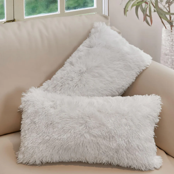 Set of two white faux fur throw pillows with fluffy texture on a modern neutral-toned couch

