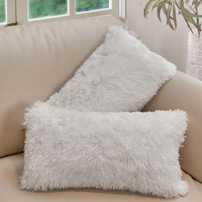 Set of two white faux fur throw pillows with fluffy texture on a modern neutral-toned couch

