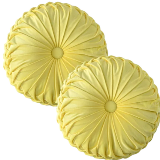 Yellow velvet round throw pillows with pleated detailing and button center, 14.5-inch set of two styled in a cozy, sunlit room.

